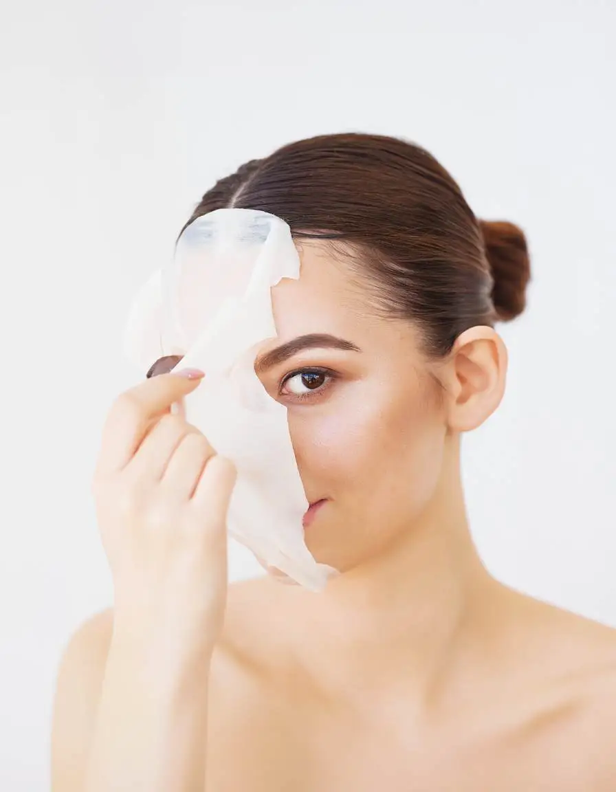 Woman removing facial mask after skin care treatment, showing radiant and hydrated skin with Crownlift